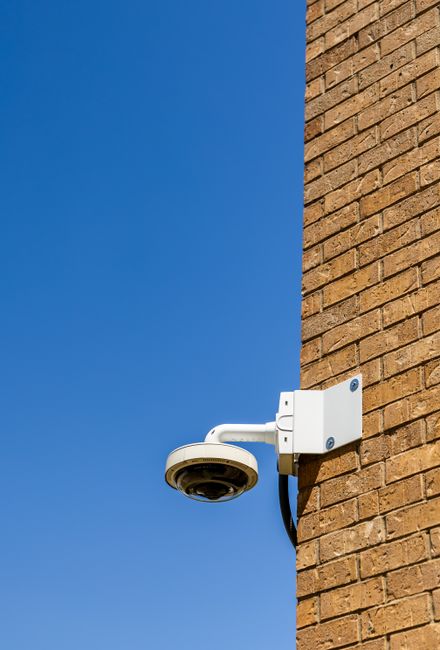 A security camera mounted on a brick wall against a bright blue sky, capturing urban surveillance.